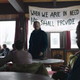 David stands before members of his congregation, a sign behind him reading When we are in need He shall provide" behind him.